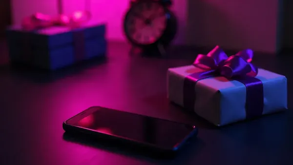 Smartphone accanto a un piccolo regalo con nastro viola, su una scrivania scura (illustrazione dell’articolo)