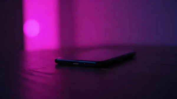 Smartphone appoggiato su un tavolo di legno scuro, circondato da riflessi viola e rosa (illustrazione dell’articolo)